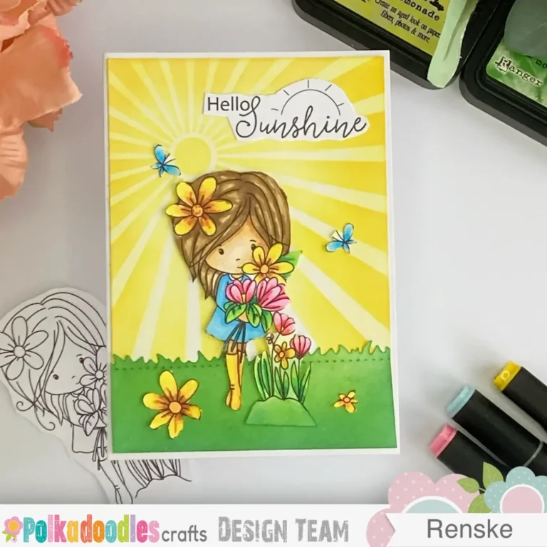 Top-down view of a easy handmade summer card featuring the Summer Dreams Winnie digital stamp from Polkadoodles. The card is laid flat and photographed straight from above. Bright yellow sunrays fill the background, with a die-cut grassy border along the bottom. The coloured image of Winnie stands in the centre holding flowers. A small sentiment reading “hello sunshine” is placed on the upper right.