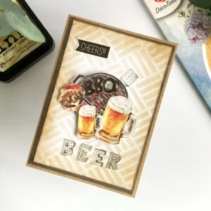 DIY Masculine Birthday card angled (1) Angled top-down photo of the masculine card showing its layered dimension. The beer and BBQ die cuts pop forward using foam tape. The stencilled distress ink background adds depth with brown tones. The vellum letters and sticker sentiment give a polished, balanced look across the card layout.