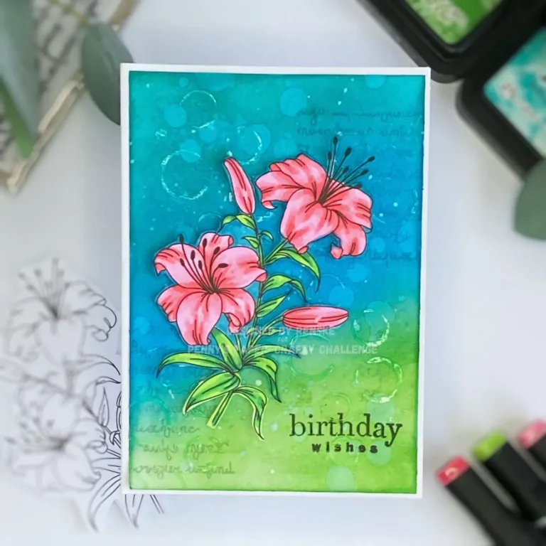 Top-down view of the flower birthday card lying flat. The card shows a blended distress ink background in blue and green tones, a delicate textured paste pattern with subtle circles, and a brightly coloured digital flower stamp placed diagonally. The stamped birthday sentiment is visible in the bottom right corner.