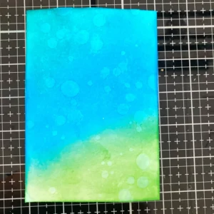 Ink blended background with distress ink Close-up of the flower birthday card background showing the distress ink blending. Peacock Feathers, Salty Ocean, and Mowed Lawn inks blend seamlessly from top left to bottom right, creating a vibrant, colourful gradient with smooth transitions and visible brush stroke