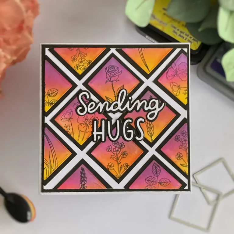 Top view of a finished geometric card placed straight in frame, featuring ink-blended squares in yellow, pink, and purple with stamped black flowers and a bold 'sending hugs' sentiment.