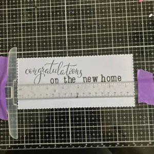 T-ruler use to line up the sentiment Slimline panel with a T-ruler used to align the stamped sentiment “on the new home” straight across the card front.
