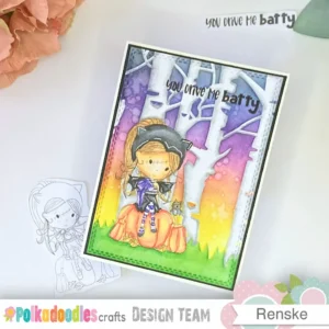 Overhead photo of the completed Halloween card using the Polkadoodles Winnie Wednesday Bat Girl digital stamp. The card is positioned at an angle to highlight the dimension and ink-blended background. Next to the card are the printed digital stamp and trimmed sentiment piece, illustrating the final stage of “how to make a Halloween card step-by-step” tutorial.