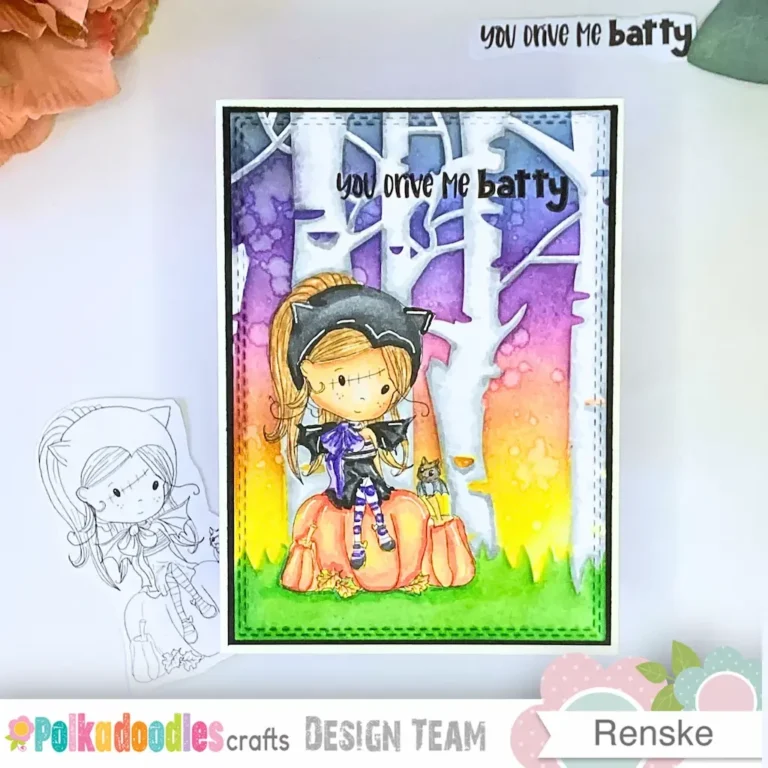 Finished handmade Halloween card featuring the Polkadoodles Winnie Wednesday Bat Girl digital stamp sitting on a pumpkin, surrounded by softly blended distress ink background with trees and grass details. The full card is photographed from above, centered in the frame, with the printed digital stamp and cut-out sentiment shown beside it — perfect visual for “how to make a Halloween card step-by-step