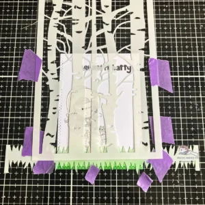 Using grass and tree stencils together to create layered ink background with mask in place — scene building in how to make a Halloween card step-by-step tutorial.