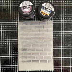 Brick wall background card with gilding wax highlights applied, two wax pots (Graphite Night and Rose Quartz) shown at the top."