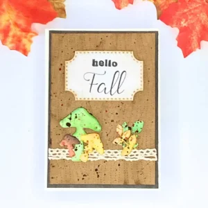 Handmade autumn card with woodgrain background, layered mushrooms, and colourful leaves, shown flat on a craft desk as part of a woodgrain background card tutorial.