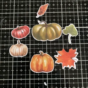 Assorted autumn die-cuts including pumpkins and leaves, ready to be layered on a brick wall background card."