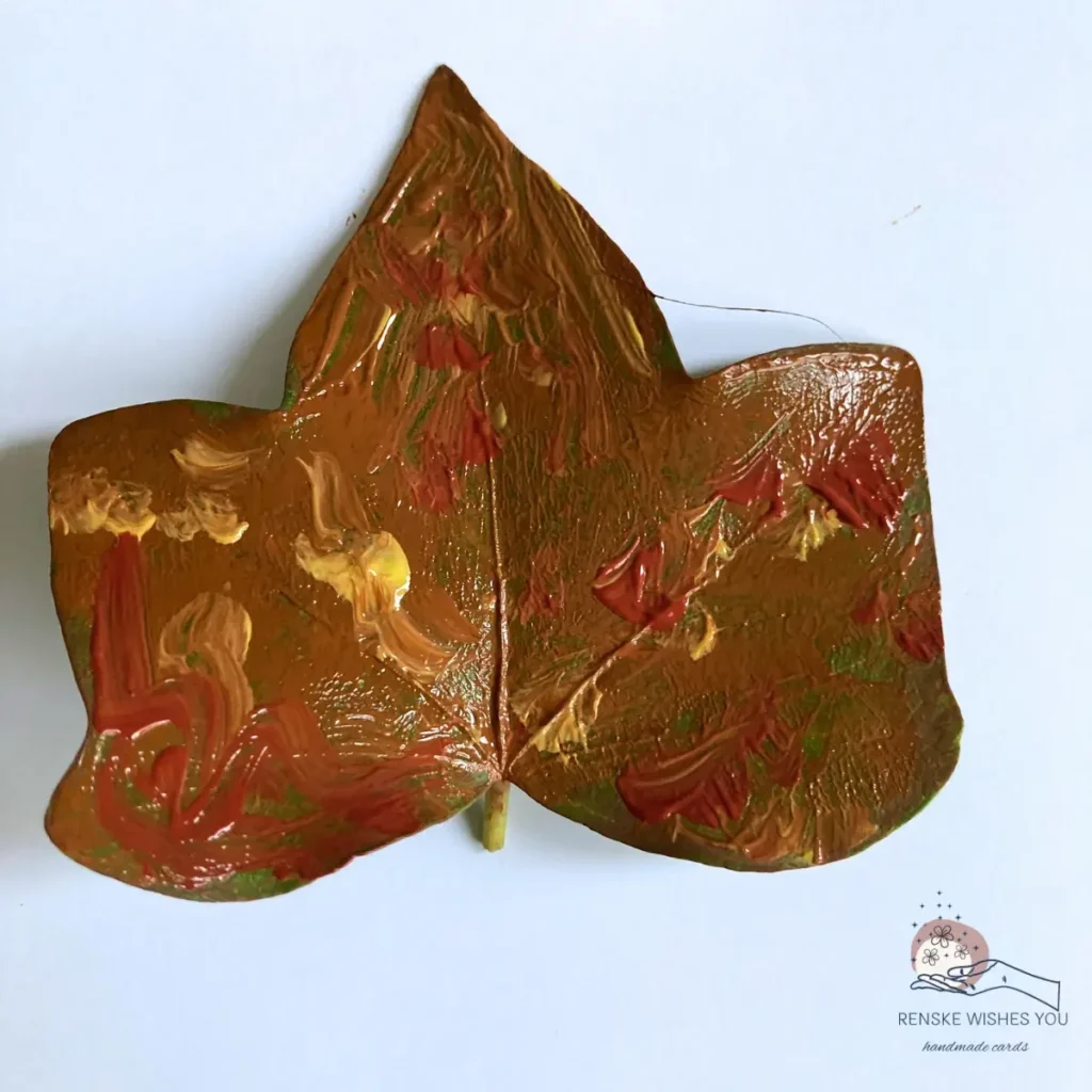 A real autumn leaf coated with acrylic paint in warm tones, ready to stamp for a leaf stamping card.