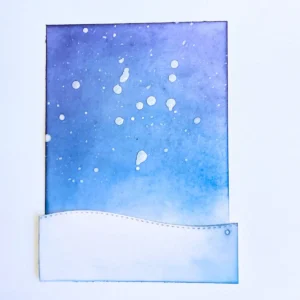 Winter Night snow sky background Blended night sky background for a winter shaker card with Distress Inks in shades of blue, white acrylic paint splatters creating falling snow, and a stitched snow hill at the bottom.