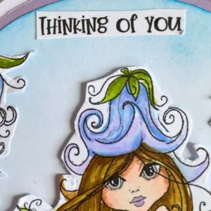 The top portion of the card features a white paper strip with the words thinking of you printed in a dark font. It is placed along the curved top edge of the arch shaped card base. The background shows a soft blue distress ink blend that looks like a calm morning sky
