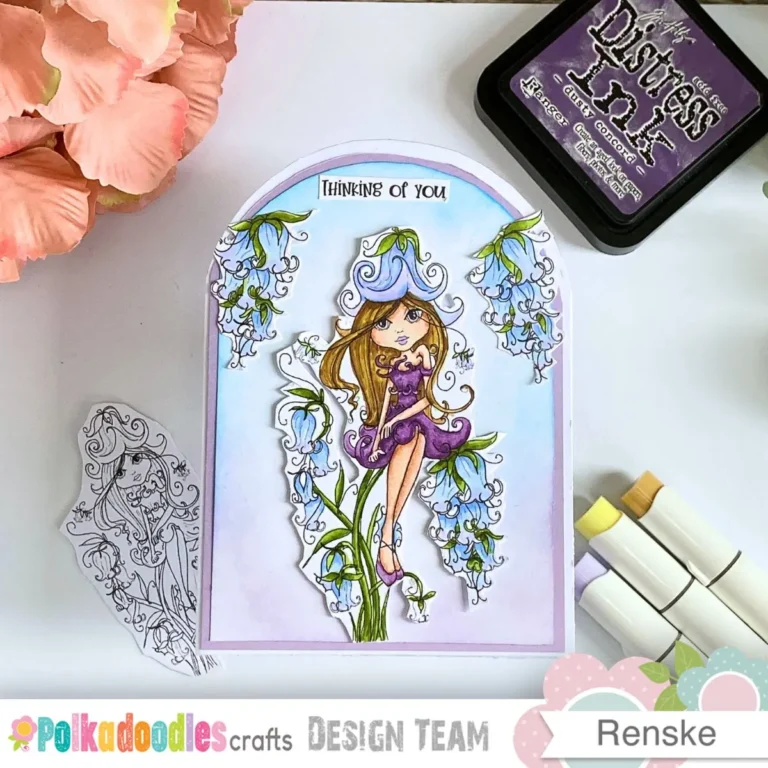 The finished floral arch shaped card is displayed with craft markers and ink pads nearby on a wooden desk. Soft lilac and white cardstock layers create a quiet frame for the central character. This design is a lovely example of a handmade thinking of you card for a friend.