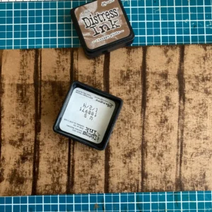 Woodgrain Background An ink cube creates vertical lines on kraft paper to build a rustic woodgrain background. This technique adds depth and character to your project without needing specialised embossing folders. Each stroke mimics the natural grain of a wooden pub table.