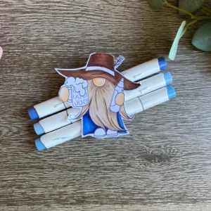 Colouring the denim coat. Detailed gnome colouring shows the denim blue tones being applied to the coat . Layering these markers helps create shadows and highlights in the fabric. This process makes the whimsical character feel real for your handmade Father’s Day card.